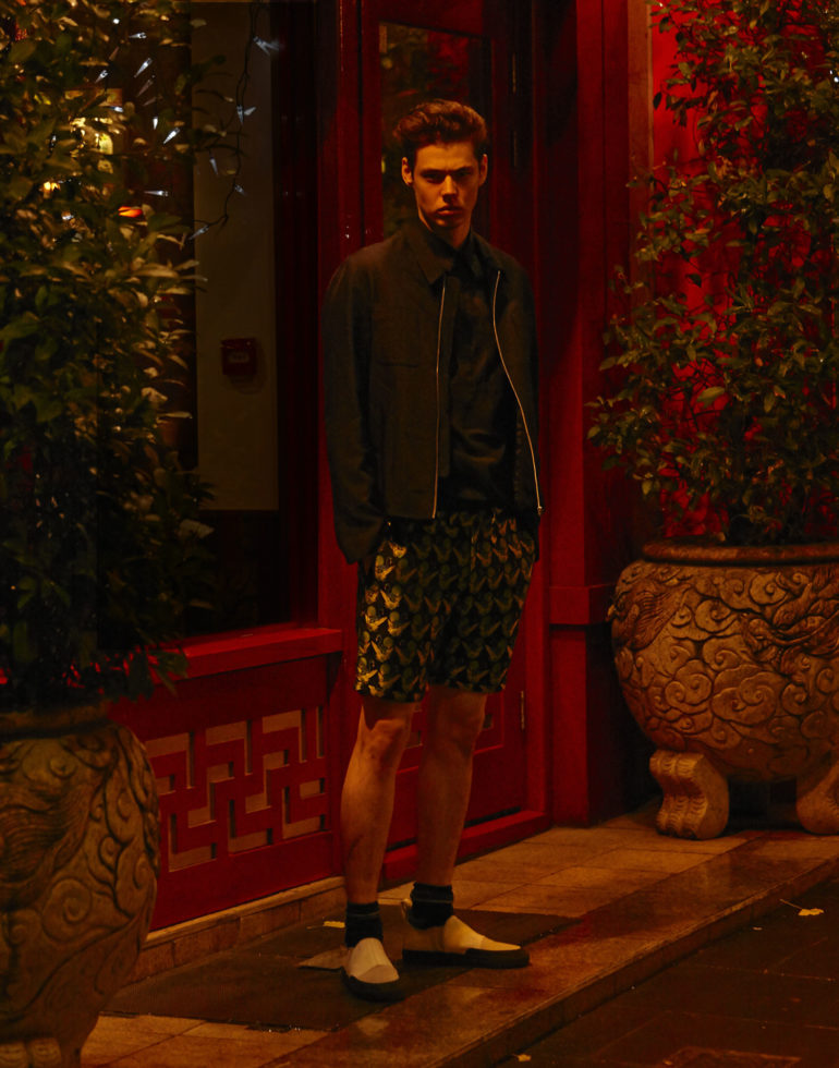Navy luxe bomber jacket MOHSIN, textured sleeveless navy shirt MOHSIN, flamingo print jacquard shorts in black, green and yellow SCOTCH AND SODA, black tiago socks FALKE, white canvas slip-on sneaker with black rubber detailing BLOOD BROTHER