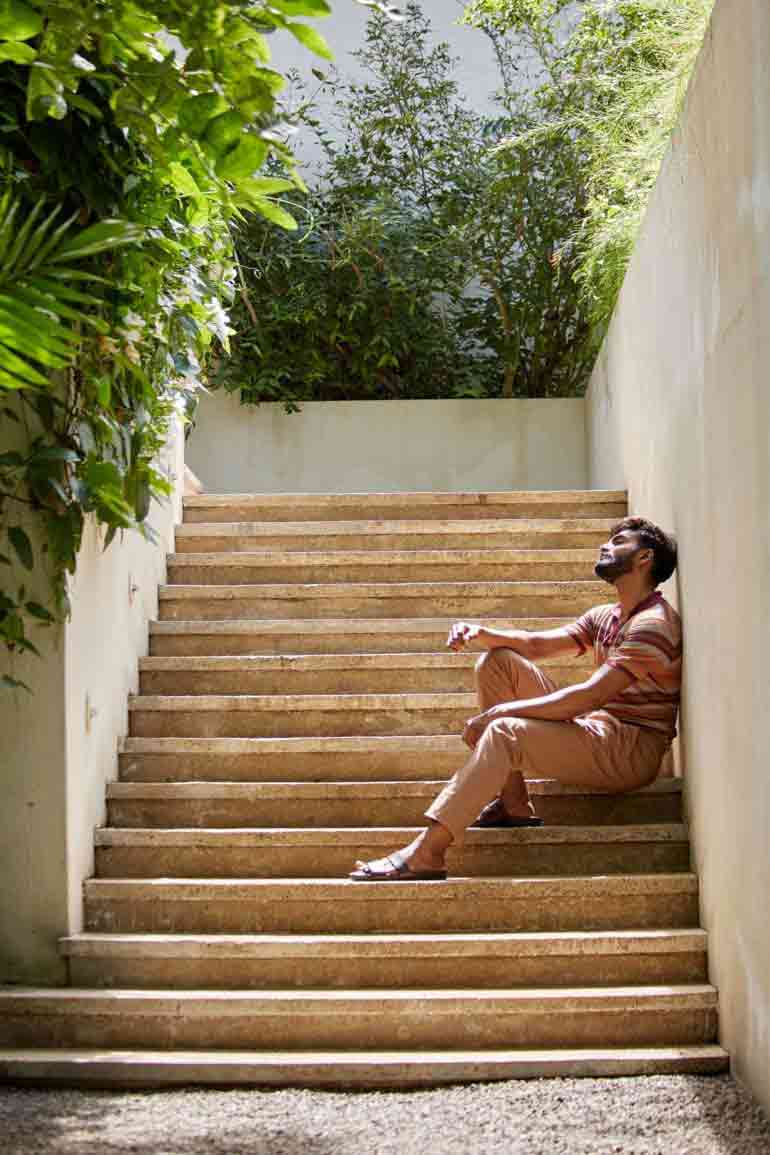 Model wearing flax striped polo shirt and cotton-and-silk trousers with drawstring waist by Corneliani and brown leather 'Chadwick' sandels by Grenson in Galle, Sri Lanka