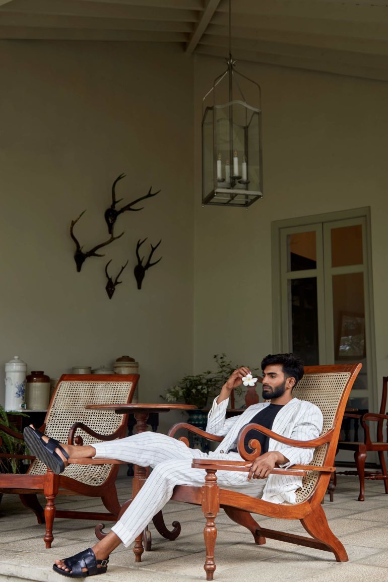 Model wearing white pinstripe single-breasted linen suit by Brunello Cucinelli, black slubbed linen jersey T-shirt by 120% LINO and black leather 'Wiley' sandels by Grenson at Amangalla, an Aman resort, Galle, Sri Lanka