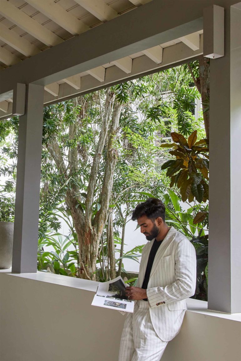 Model wearing white pinstripe single-breasted linen suit by Brunello Cucinelli, black slubbed linen jersey T-shirt by 120% LINO and black leather 'Wiley' sandels by Grenson at Amangalla, an Aman resort, Galle, Sri Lanka