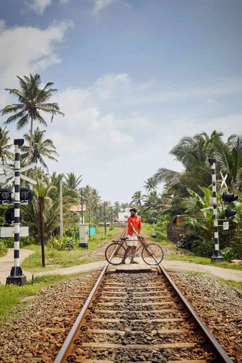 Model wearing red linen shirt by Vilebrequin, cream cotton drawstring shorts by Brunello Cucinelli and brown leather 'Chadwick' sandels by Grenson in Galle, Sri Lanka