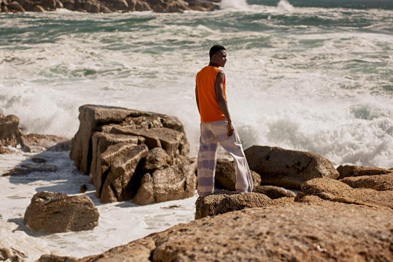 Model wearing tie-dye lavender stripe painter pants by Ullac Oy and orange brushed cotton 'Le Sports Vest' by Les Basics in Bantry Bay, Cape Town, South Africa
