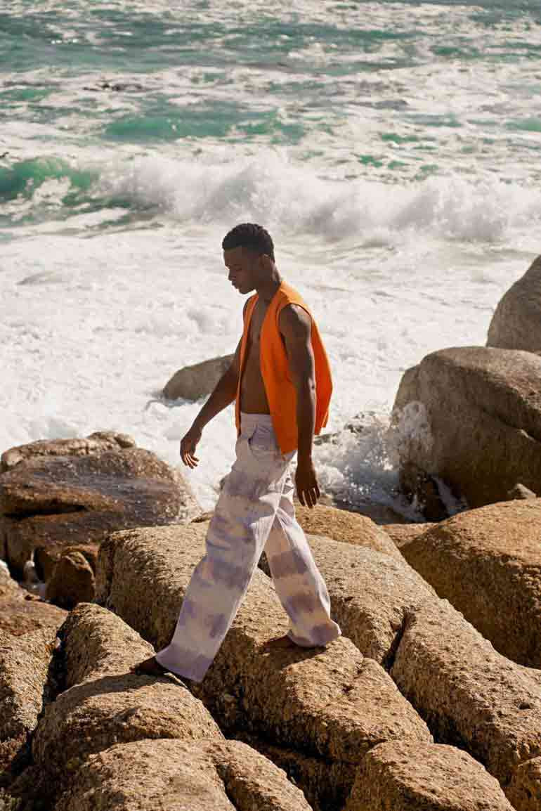Model wearing tie-dye lavender stripe painter pants by Ullac Oy and orange brushed cotton 'Le Sports Vest' by Les Basics in Bantry Bay, Cape Town, South Africa