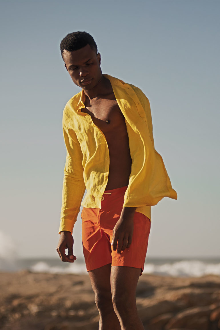 Model wearing yellow linen shirt by Vilebrequin and 'Standard Dark Papaya Mid-Length Swim Shorts' by Orlebar Brown in Bantry Bay, Cape Town, South Africa