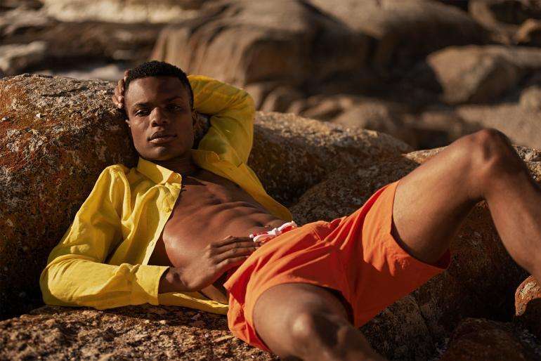 Model wearing yellow linen shirt by Vilebrequin and 'Standard Dark Papaya Mid-Length Swim Shorts' by Orlebar Brown in Bantry Bay, Cape Town, South Africa