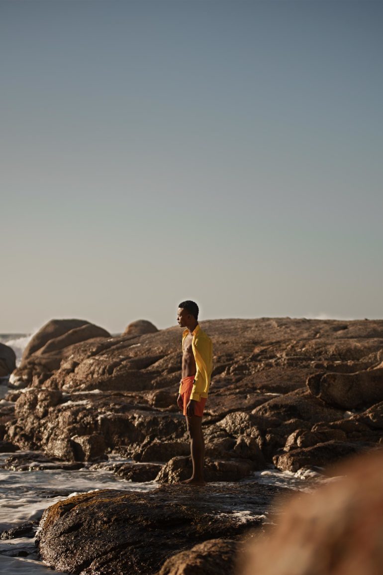 Model wearing yellow linen shirt by Vilebrequin and 'Standard Dark Papaya Mid-Length Swim Shorts' by Orlebar Brown in Bantry Bay, Cape Town, South Africa