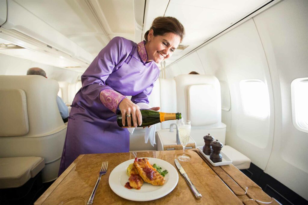 A flight attendant serving lunch and a glass of champagne aboard the Abercrombie & Kent Private Jet