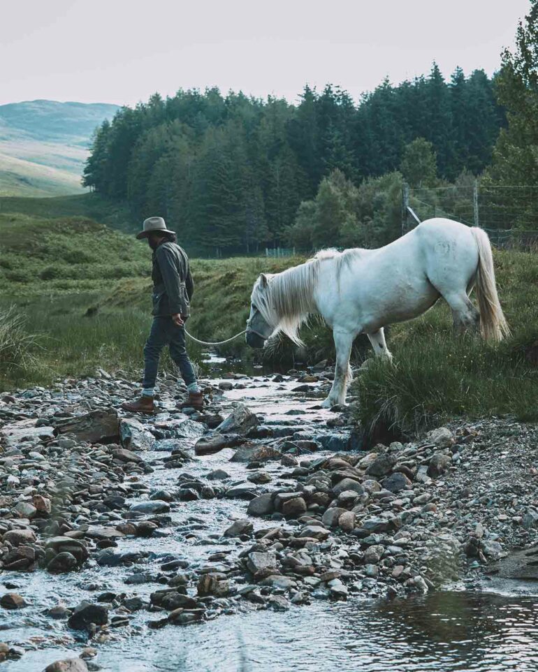 Model and horse traverse a stream in Glen Artney, Scotland