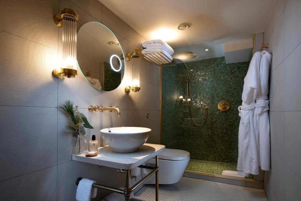A stylish bathroom with a circular mirror and shower with green tiles.