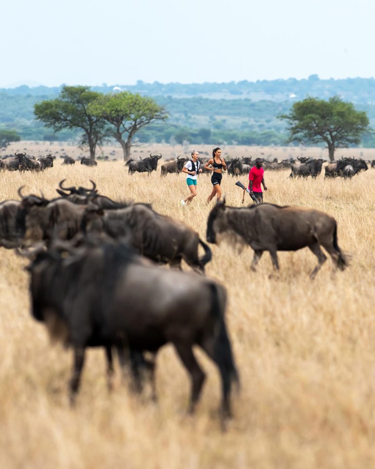 Accompanied by a ranger, women jog among wildebeest in the Grumeti Game Reserve, Tanzania