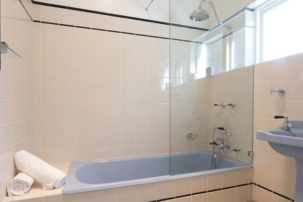 A periwinkle bathtub with white tiles and rolls of towels
