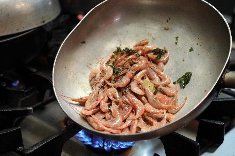 Shrimp being cooked in a frying pan with herbs