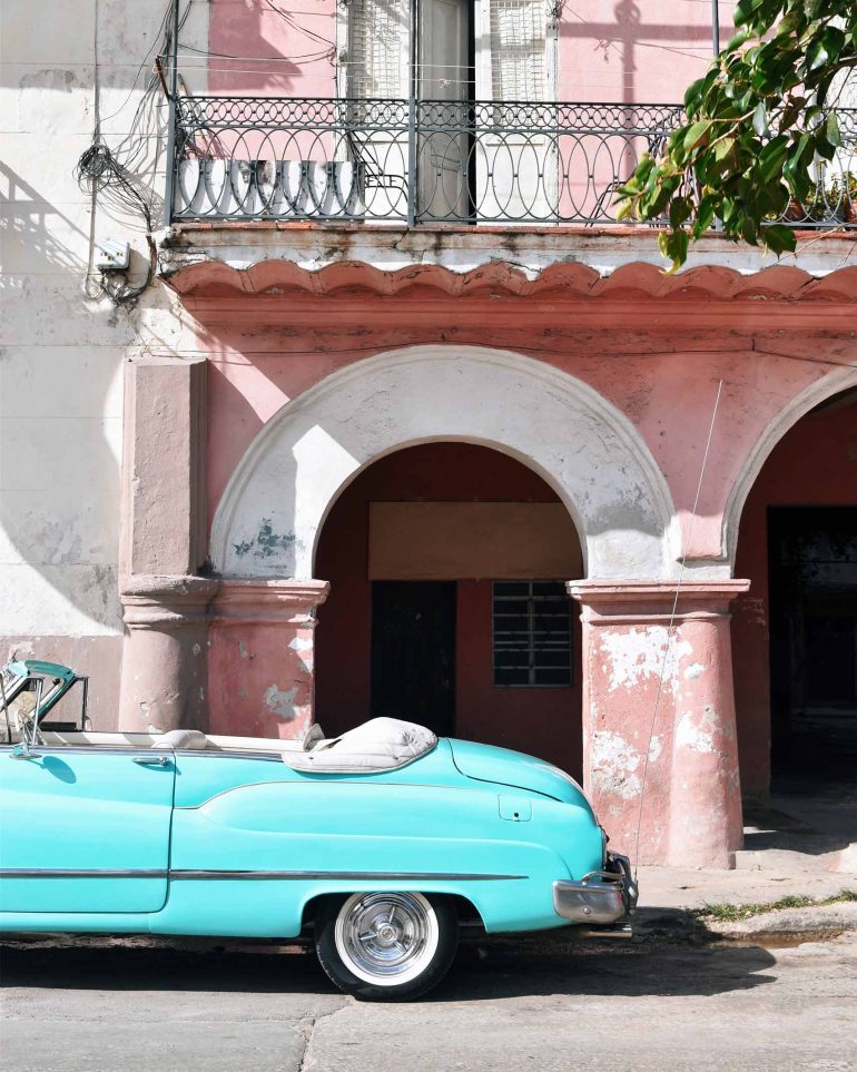 A vintage car is parked outside a pink house in Havana, Cuba