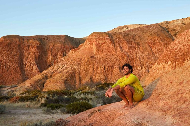 Model Nathan McGuire kneeling in a landscape during sunset, South Australia menswear editorial, Australia