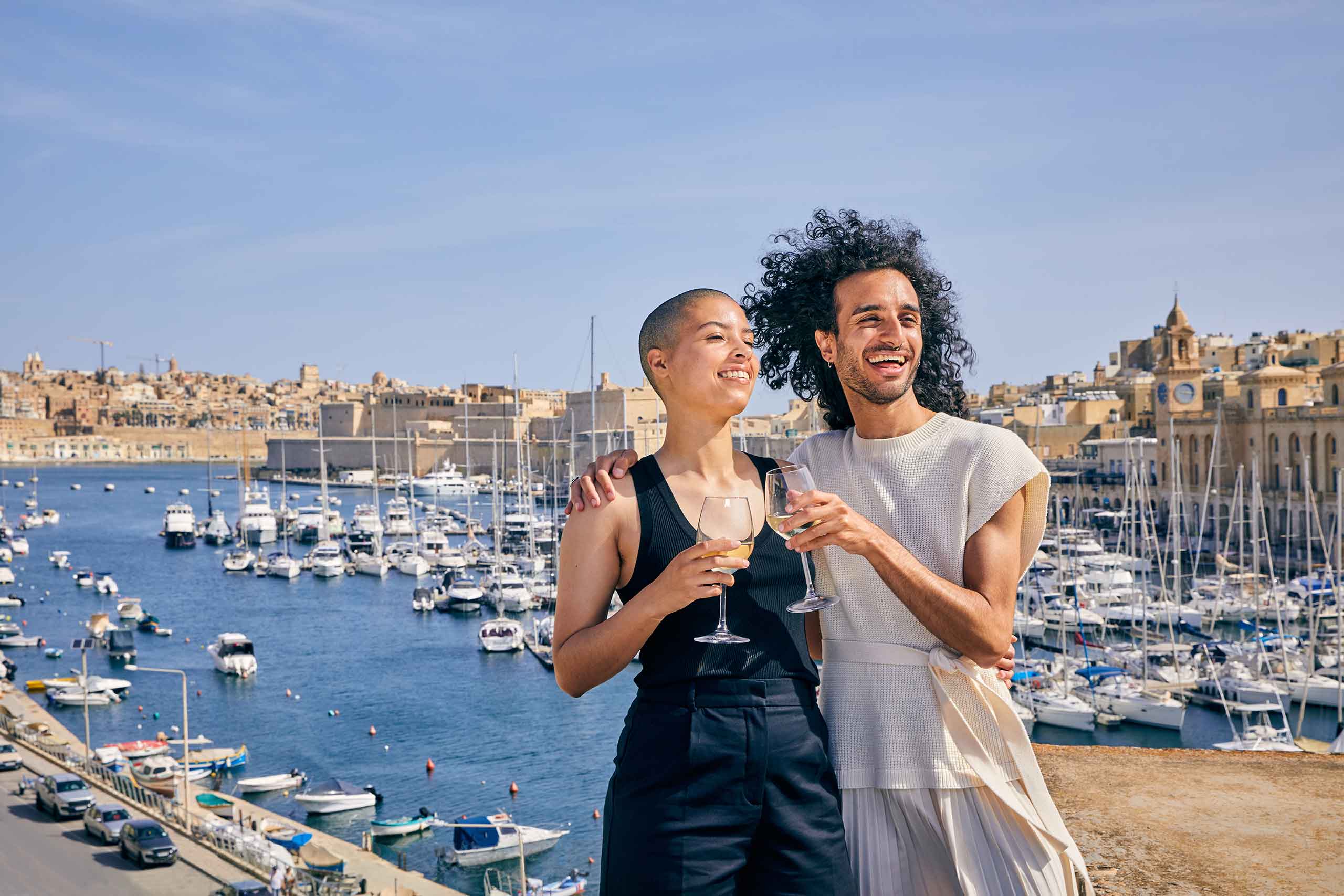 Non-binary couple enjoying a drink and view over the rooftop of the Three Cities and Valletta in Malta