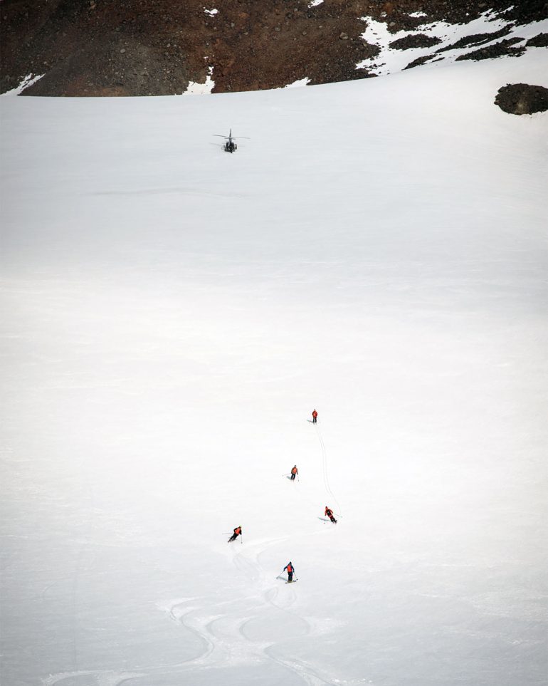 A group of heli-skiers make their way down a mountain as their helicopter flies above, Swedish Lapland, Sweden