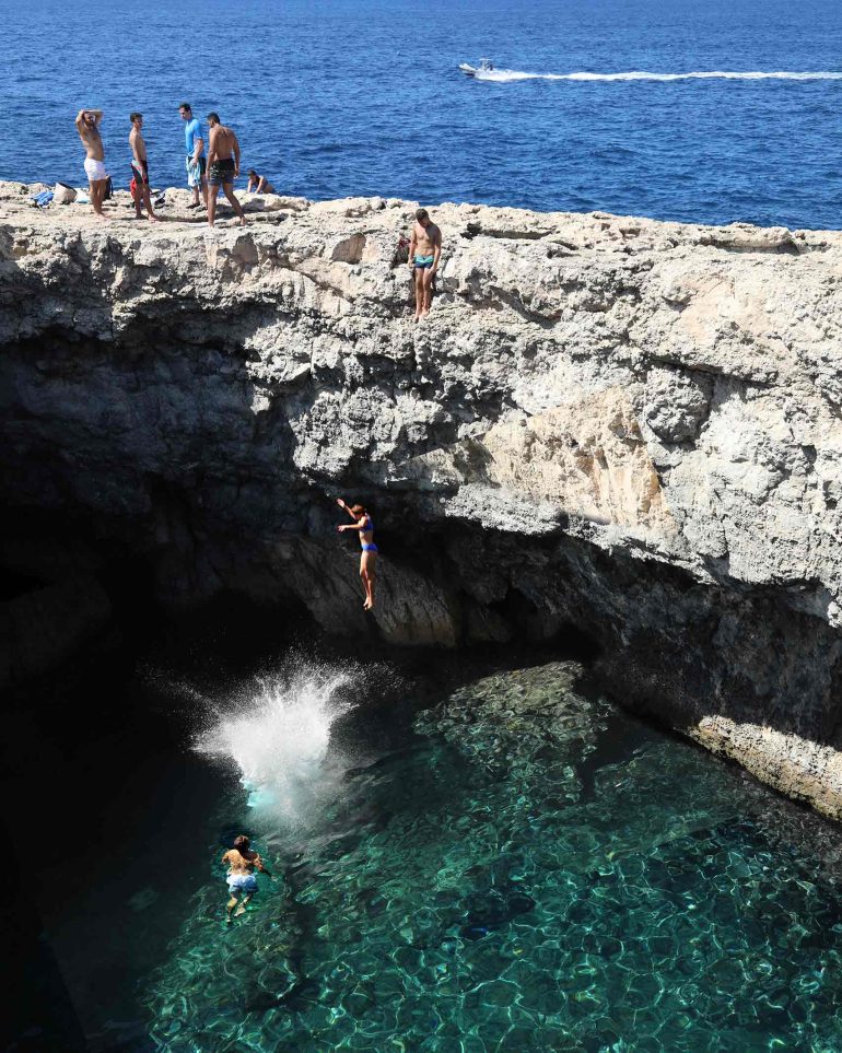 Young locals jump into the Mediterranean sea from small limestone cliffs
