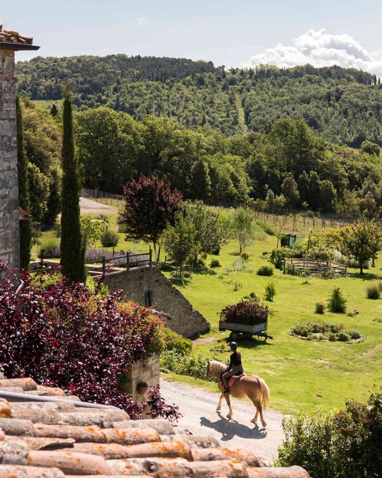 A hotel guest rides a horse on the grounds of Borgo Pignano, Tuscany, Italy