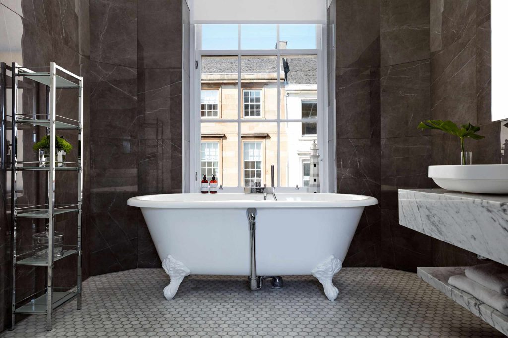 A bathroom with a freestanding bathtub and views of Glasgow at Kimpton Blythswood Square, Glasgow, Scotland.