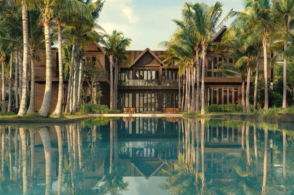 External views of the Kimpton Kitalay Samui shrouded in palm trees with a still turquoise pool in the foreground