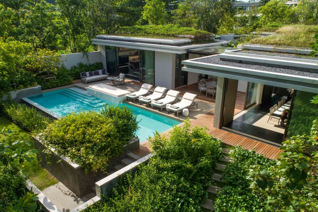 External view of Rosewood Phuket nestled into green hills. A pool with sun loungers can be seen.