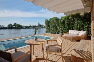 An outdoor lounge space with a pool that fringes the Chao Phraya River at A plush green outdoor communal space at Sala Bang Pa-In Ayutthaya, Thailand