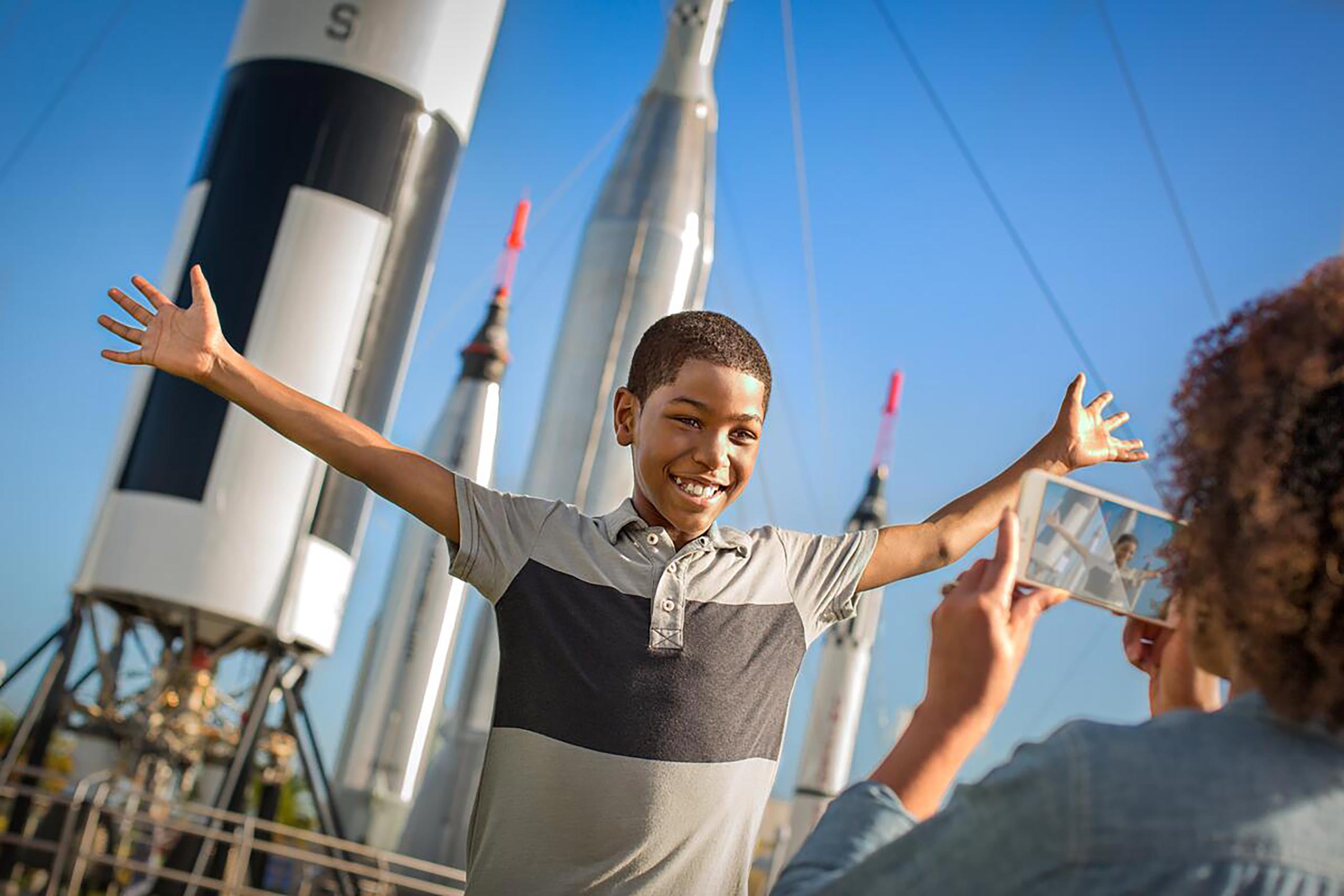 A young boy having his picture taken in front of rockets and enjoying the accessible experiences at the Kennedy Space Center.