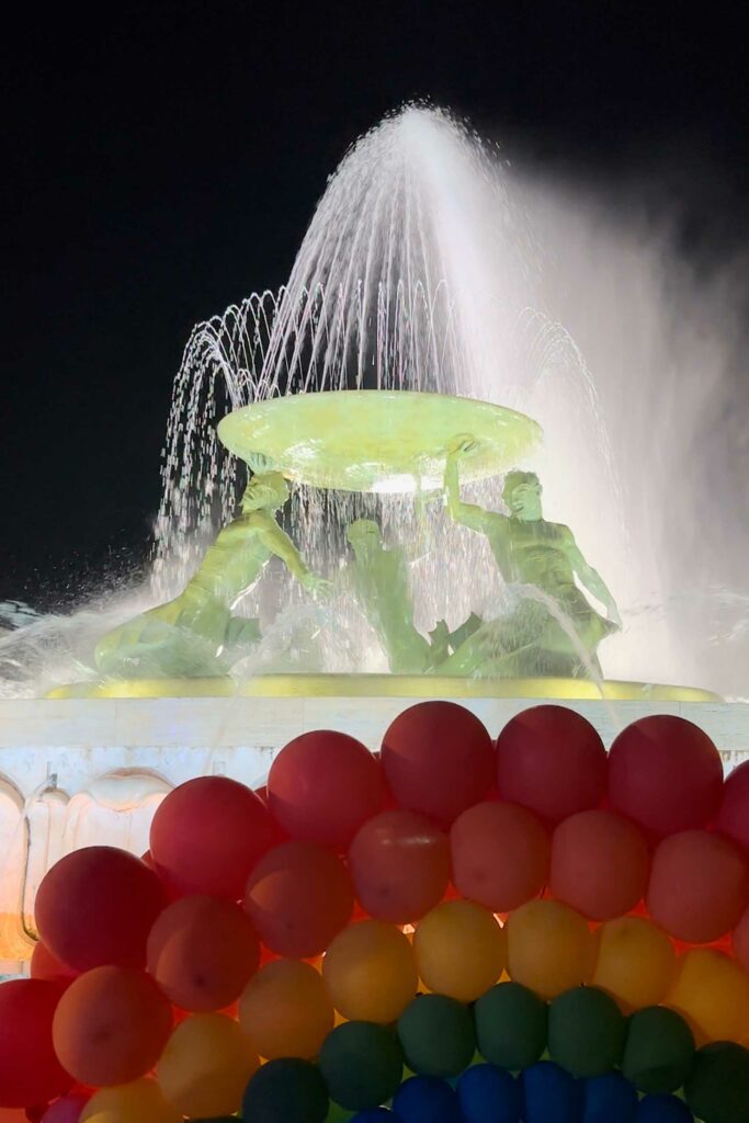 A water sculpture behind rainbow balloons.