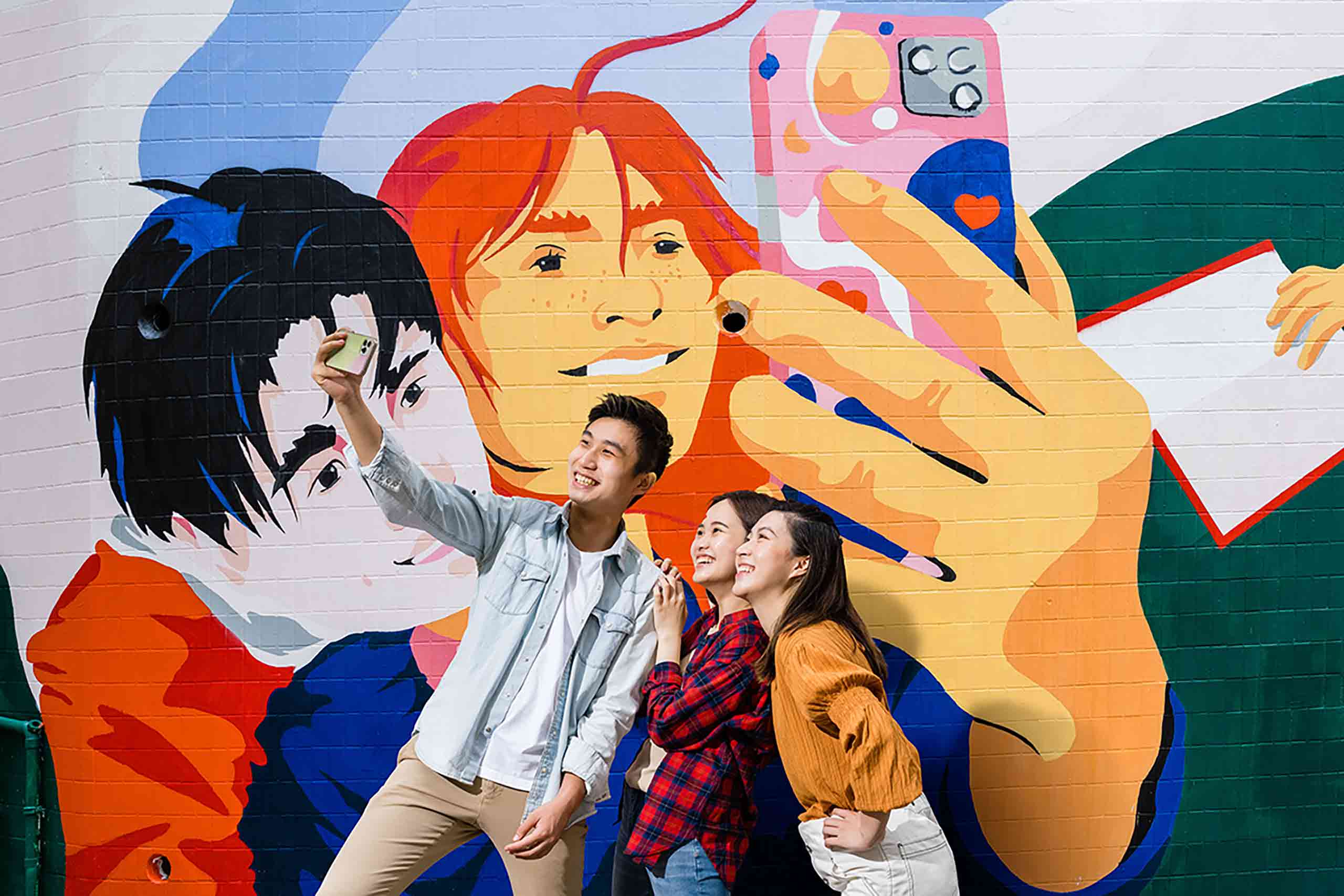 A young group of friends take a selfie in front of an art mural.