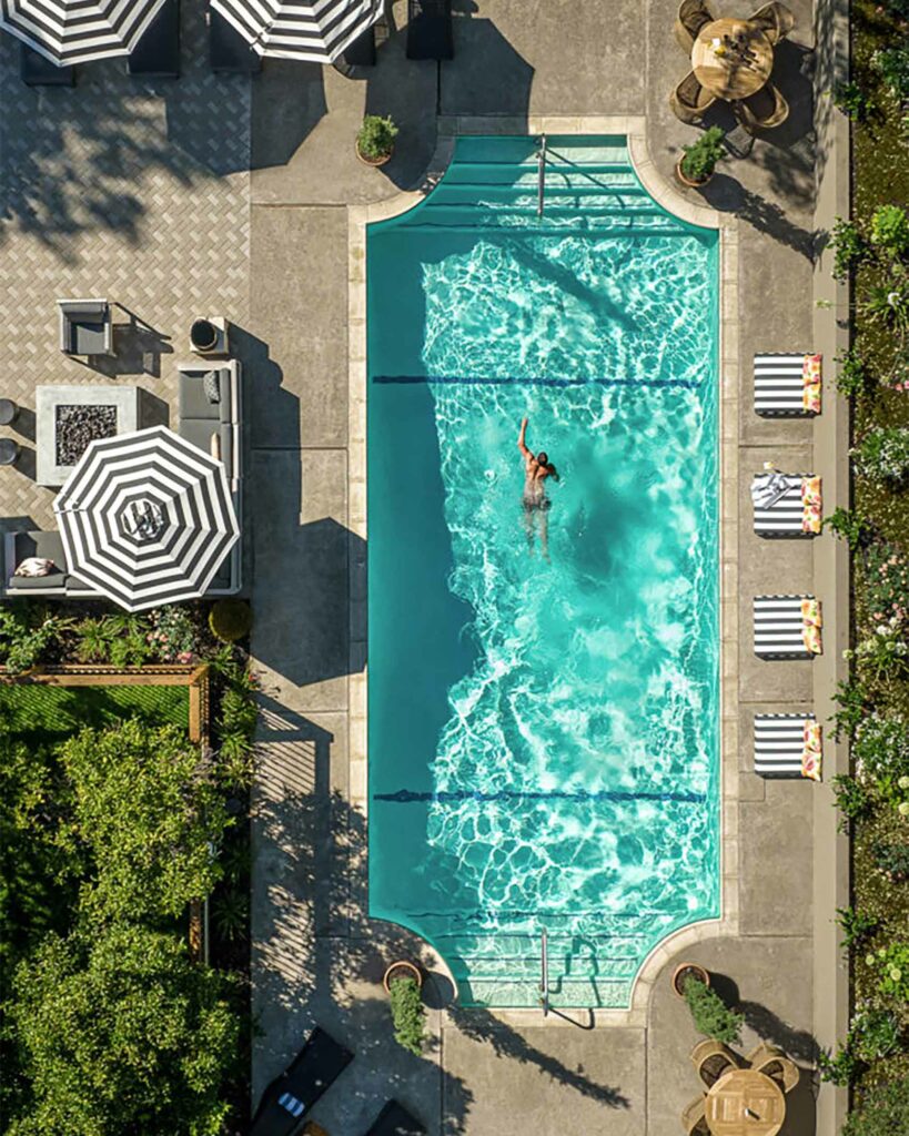 Outdoor swimming pool from a birds-eye view with a man swimming in it.