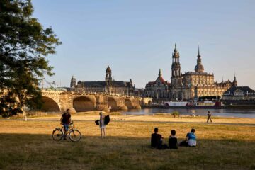 Locals sit in the grass by the Elbe, observing the skyline of Dresden, Germany