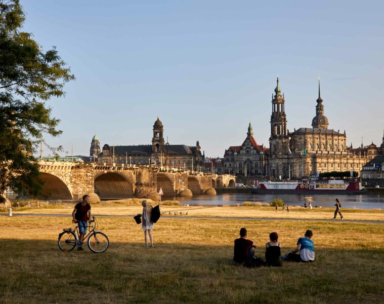 Locals sit in the grass by the Elbe, observing the skyline of Dresden, Germany