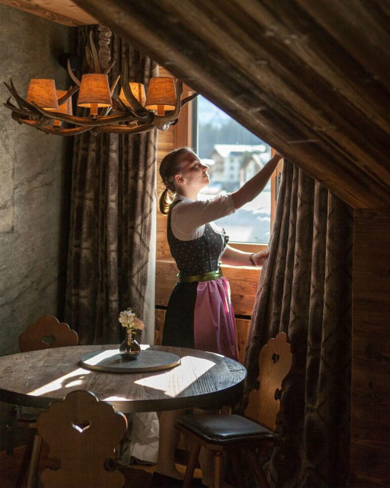 A staff member rearranges the curtains in a guest room at Hotel Arlberg, Lech, Austria