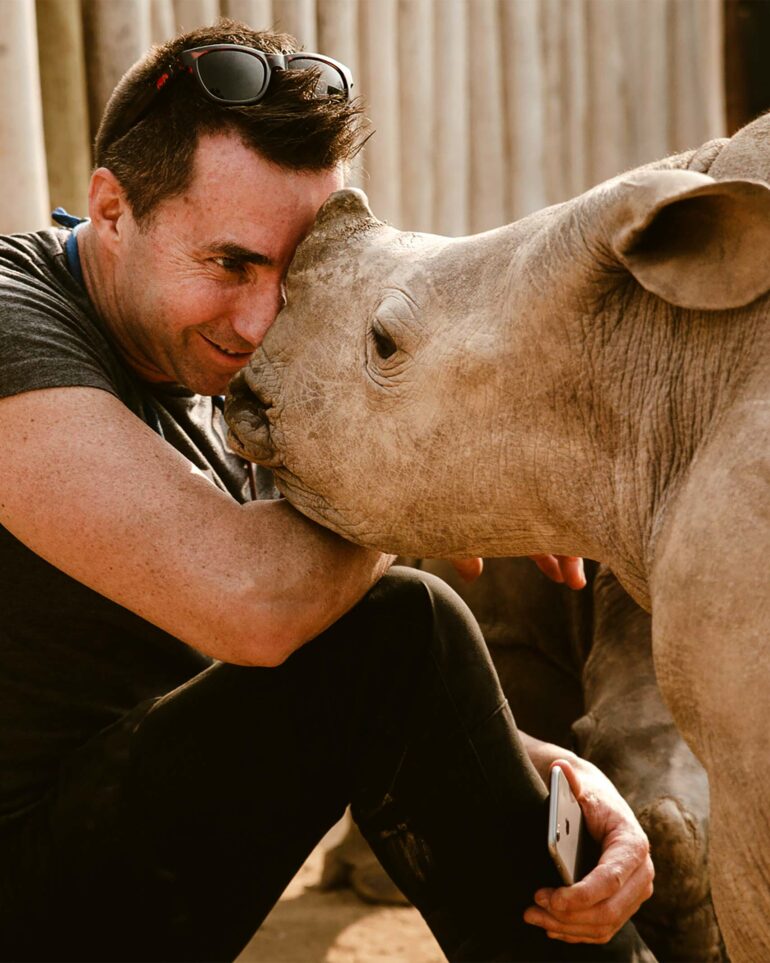 David Ryan gently touches the face of a baby rhino with his forehead in South Africa