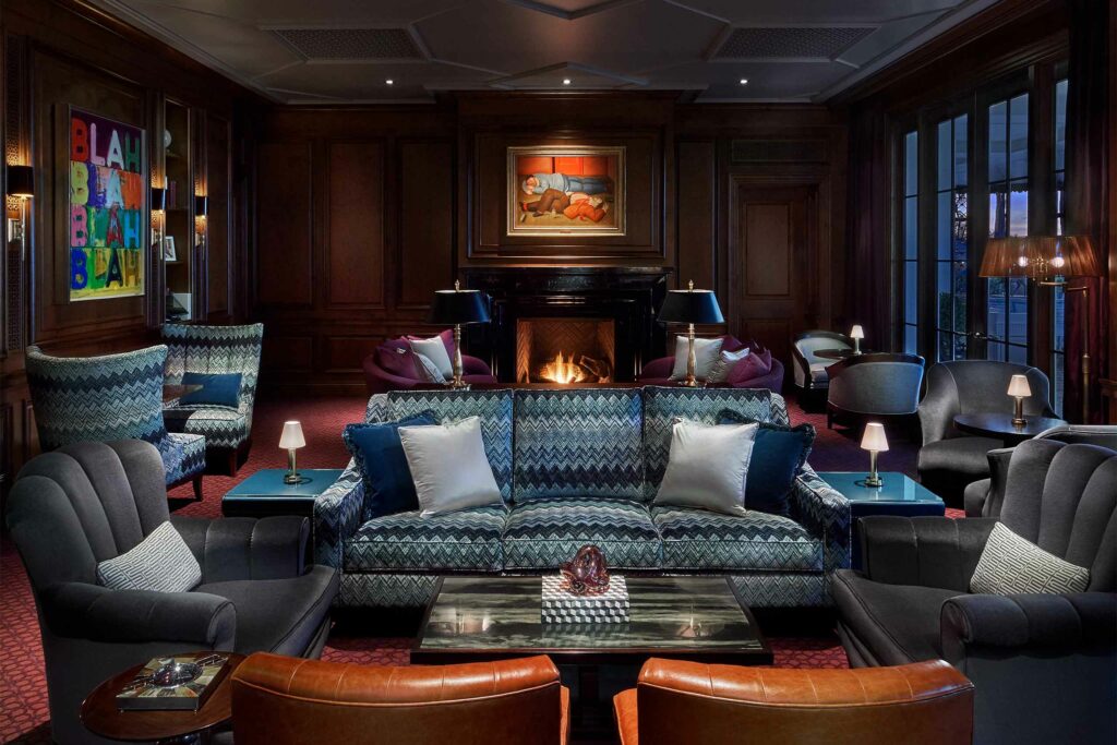 A dimly lit Manor Bar with dark wood furnishing and a fireplace at Rosewood Miramar Beach.