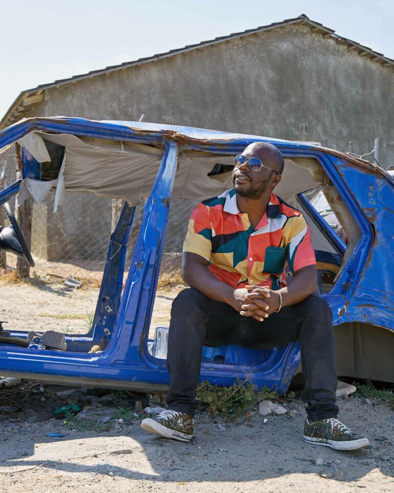 Juma Mkwela of Juma Art Tours poses for a picture in a discarded car, Cape Town, South Africa