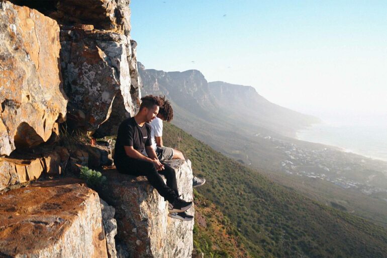 Hikers sits on a rock's edge looking out over the sea, Cape Town, South Africa