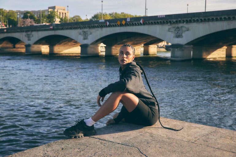 Koko Barno poses in front of a bridge along the Seine in Paris, France