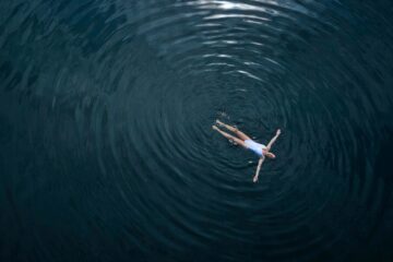 A woman in a white bathing suit bathes in dark blue water that ripples away from her
