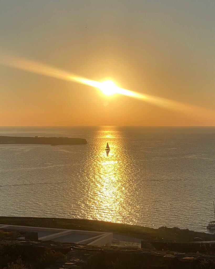 Sunset over the Aegean sea, with a sailboat floating in its glow