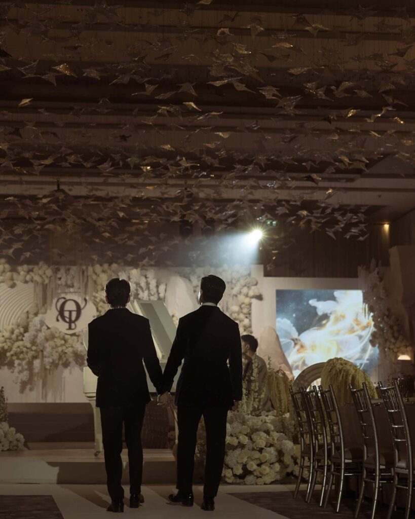 Two men stand hand in hand at the front of their wedding venue. LGBTQ+ Weddings at Capella Bangkok