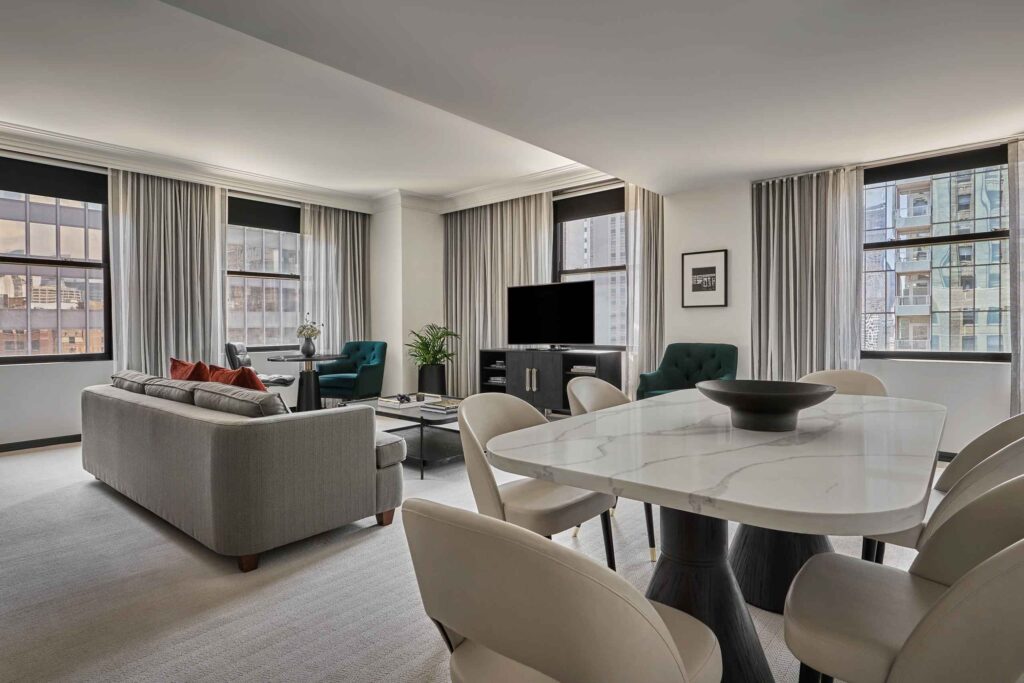 Clean living room space, in a corner suite at Pendry Chicago, with marble dining table and six chairs and lounge area