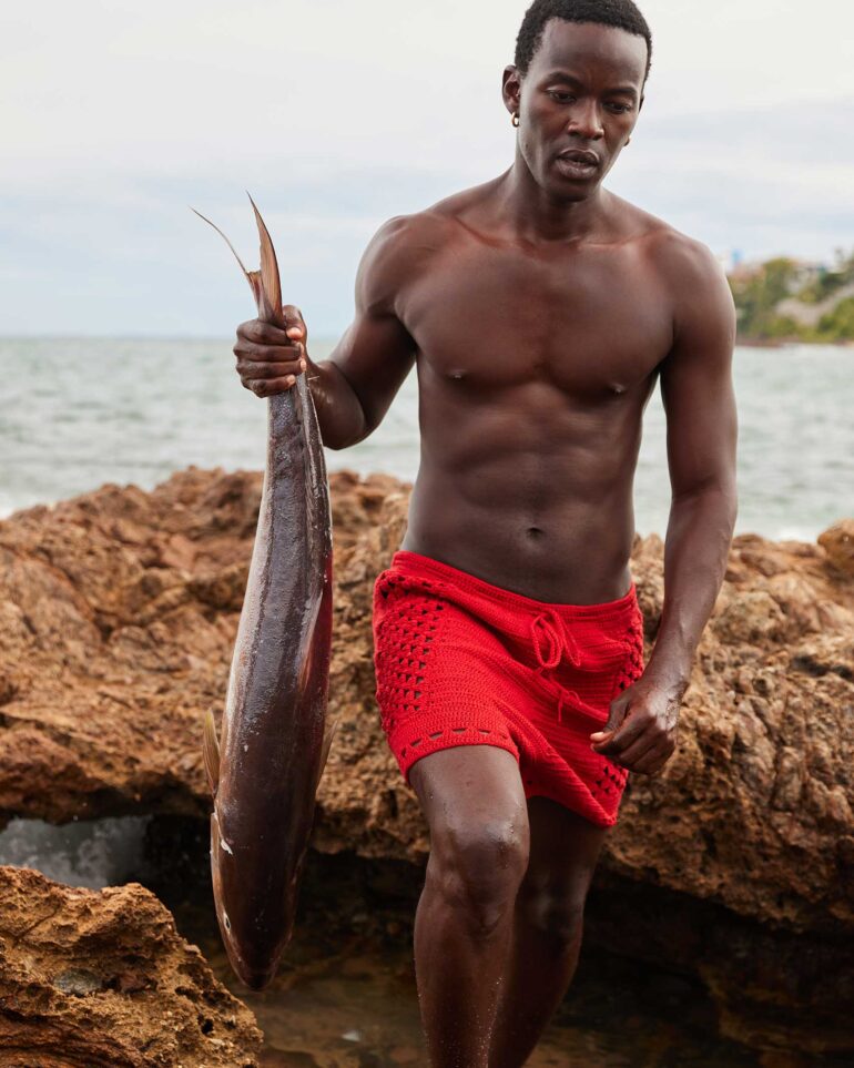 Fah Sampaio walks towards the camera while holding a fish in Salvador, Brazil