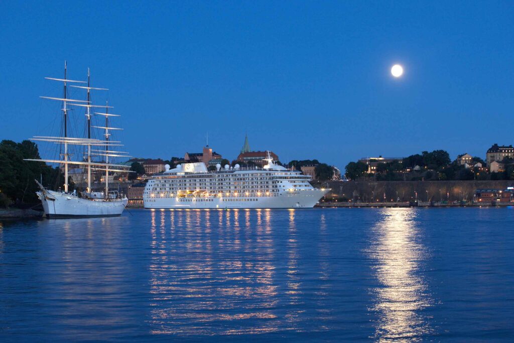 Cruise into the Open City – cruise ship docks in Stockholm next to an old sailing boat, with a full moon reflecting in the water