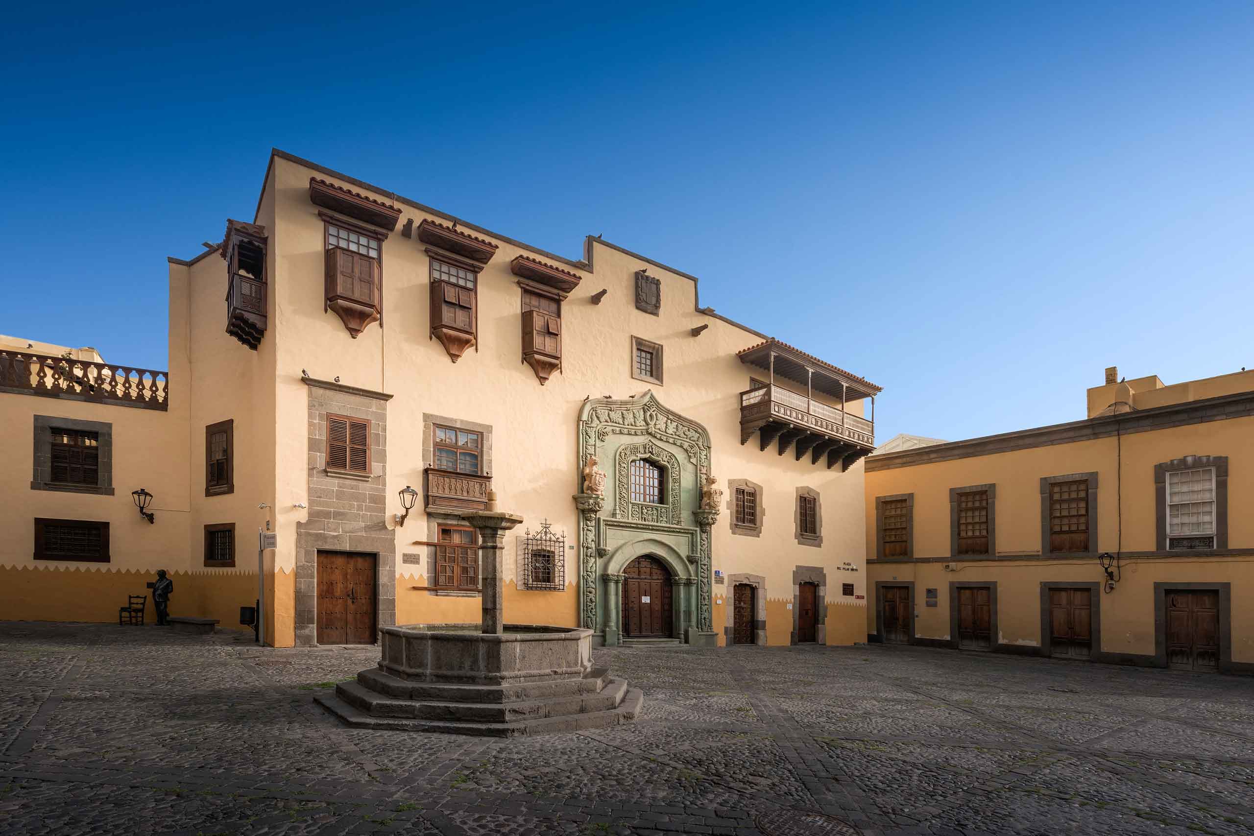 A colonial architecuture building in Las Palmas, Gran Canaria. It is big, yello and has an intricately carved green arch over the door as well as wooden balconies