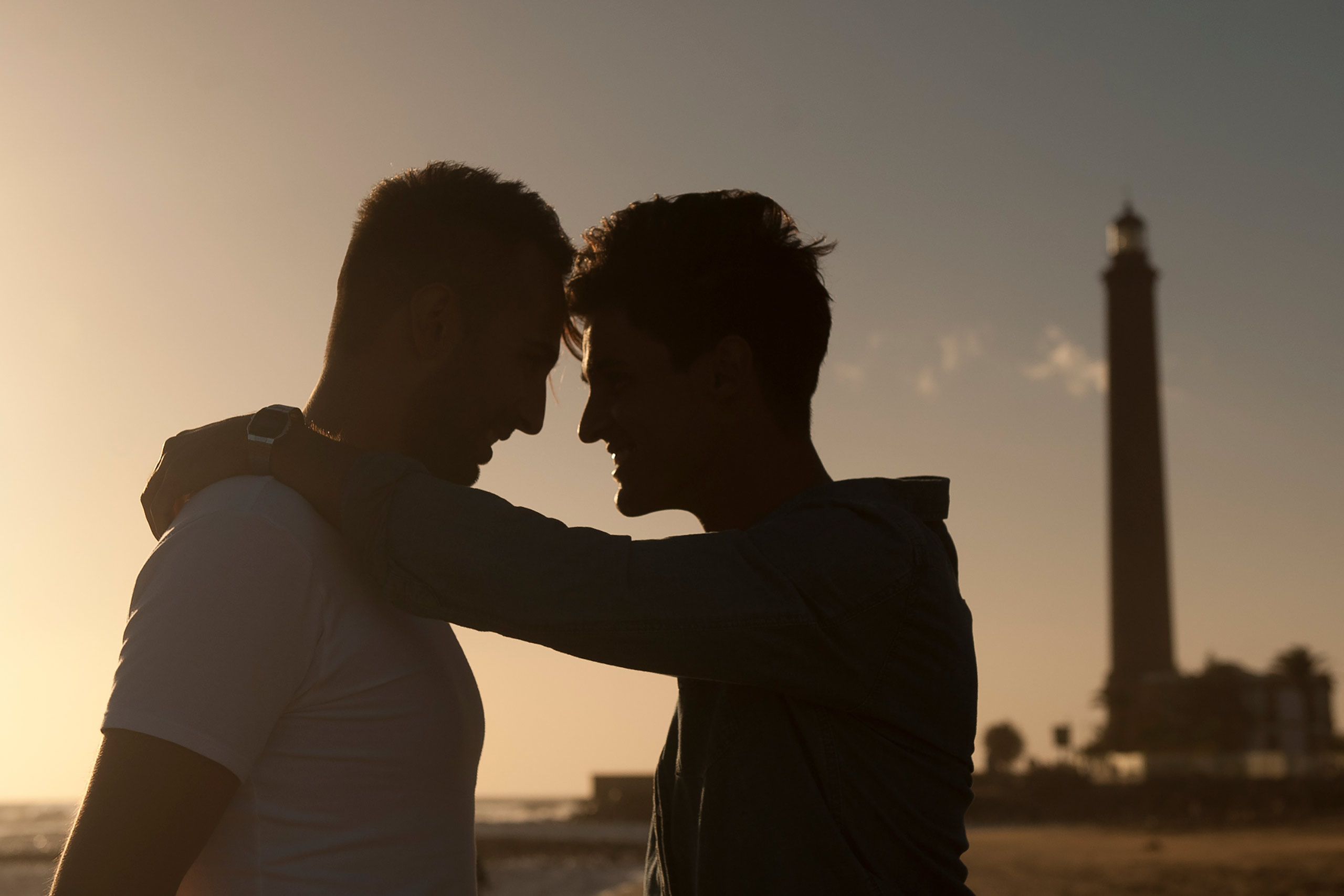 Silhouette of two men embracing with a lighthouse in the distance