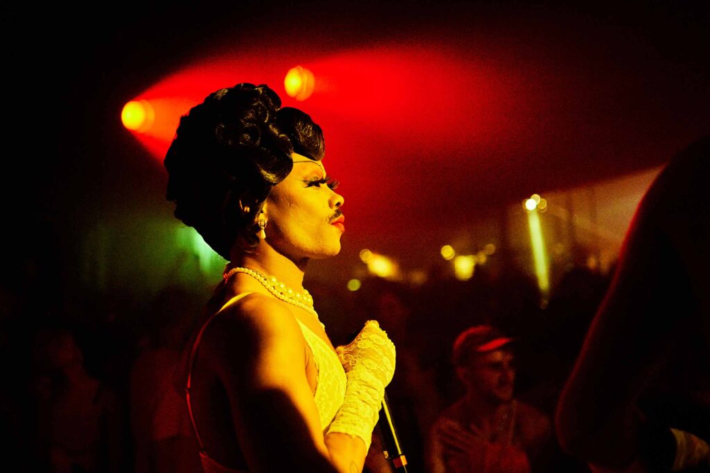 A black drag queen in a vintage wigm pearls and lace costume performs