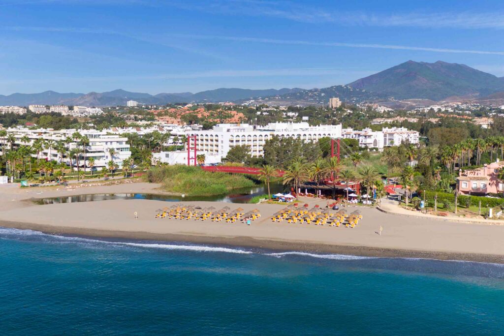 ME Marbella drone shot from the sea, showing the complex, a red suspension bridge and yellow sun loungers
