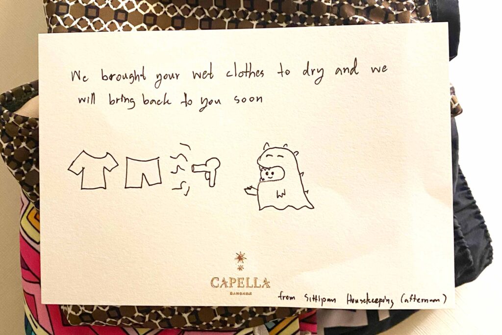 A handwritten note stacked on top of a pile of clothing that reads, "We brought your wet clothes to dry and we will bring back to you soon" with a cute little illustration of a monster drying clothes