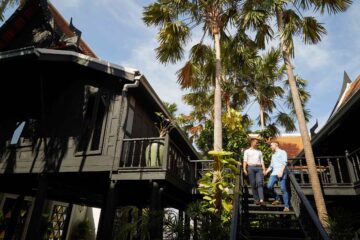 Two men, holding hands as they descend the staircase of an old teak Thai-style house in the compounds of The Siam hotel in Bangkok